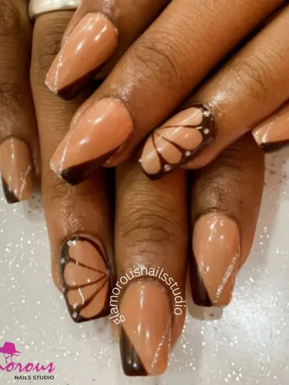 This design is inspired by the delicate beauty of a butterfly. We used a nude base with dark brown tips and created accent nails with hand-painted butterfly wings, complete with tiny rhinestone details.