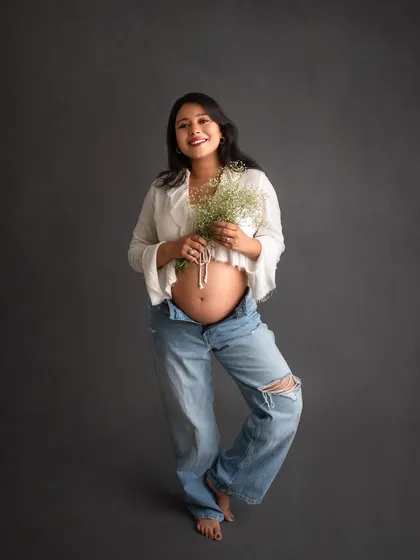 Your maternity shoot should feel like you. For a modern and relaxed vibe, we can go for a simple look like this, with a crop top and jeans against a clean backdrop, letting your beautiful bump be the star.