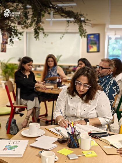 An educator takes detailed notes during a workshop, surrounded by books and resources. Our sessions are designed to be deeply informative, providing practical frameworks and strategies that can be applied immediately in the classroom or at home.