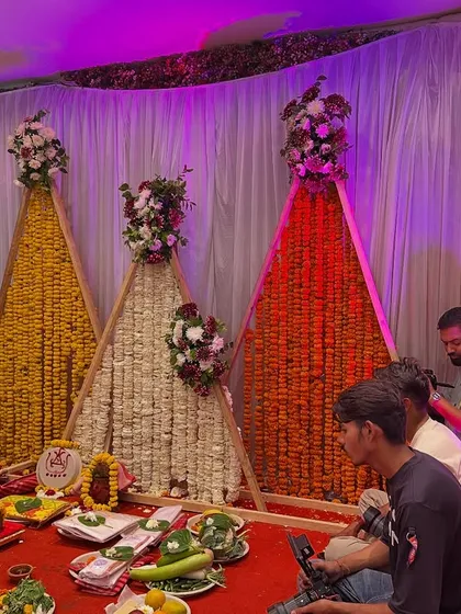 A unique and modern pooja or ceremony backdrop. This design features A-frame structures filled with marigold and tuberose (rajnigandha) garlands, topped with fresh flower bouquets.