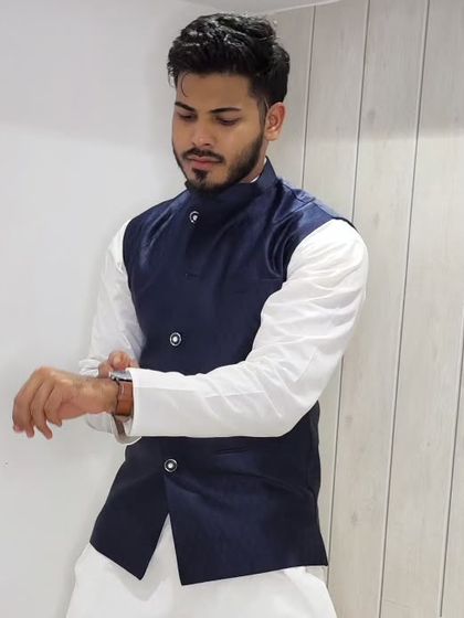 A client adjusting his cuff while wearing the navy blue jacket and white kurta set.