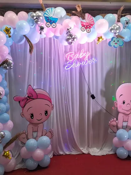 A classic pink and blue baby shower backdrop with a neon sign, sheer curtain, and cute baby character cutouts.
