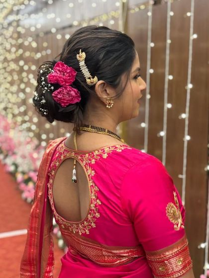 A classic Maharashtrian bridal bun. This intricate updo is adorned with fresh pink flowers and a traditional hair accessory, providing an elegant and secure base for the dupatta.