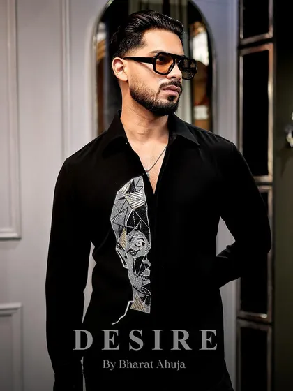 Wearable art for the modern man. This black shirt features a striking abstract face embroidered in geometric lines of silver and gold thread, creating a look that is both artistic and powerful.