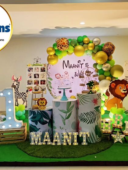 A "Wild One" jungle party setup with a circular backdrop and themed plinths. The decor includes a light-up number '1' and marquee letters spelling out the birthday boy's name.