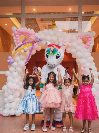 The birthday girl and her friends posing with a unicorn mascot, all raising their hands in celebration.