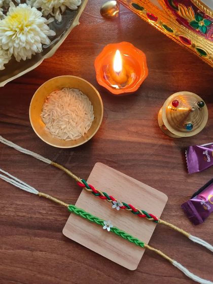 These braided rakhis are a unique option for the festival. They are available in a green braid and a red-and-green braid, each with a small floral charm.