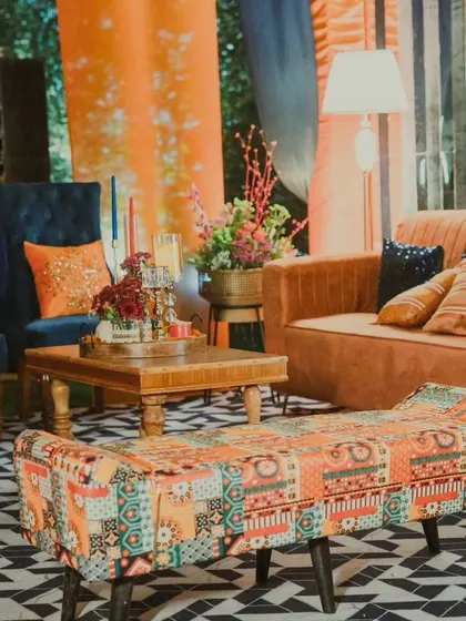 I love mixing textures and colours to create inviting spaces. This lounge area combines deep blue velvet chairs with a warm tan sofa and a vibrant patchwork bench, all set against a bold orange backdrop for a truly unique look.
