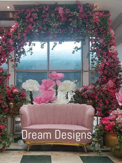 A fabulous backdrop for a Mehendi ceremony, bursting with color. A lush arch of pink bougainvillea and oversized paper flowers in shades of pink and white frames a vintage-style pink sofa.