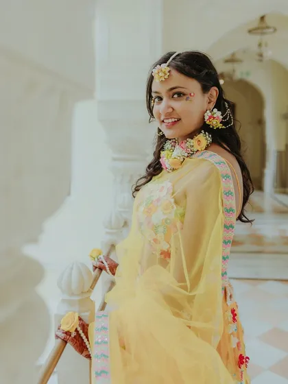 A lovely portrait of the bride, adorned with floral jewelry, smiling brightly during her Haldi ceremony.