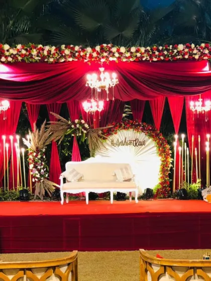 A dramatic reception stage in red and gold, featuring a personalized backdrop, elegant draping, and candelabra-style lighting.
