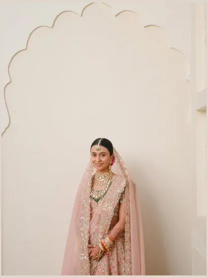 Simplicity and grace. Using a clean white wall with a traditional scalloped arch, I created a minimalist backdrop that puts the focus entirely on the bride's soft pink Anamika Khanna lehenga and her serene expression.