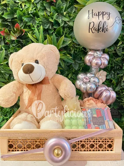 This Rakhi, send a whole vibe. This adorable gift basket includes a teddy bear, treats, and a custom "Happy Rakhi" balloon bouquet in a stylish silver and lilac palette.