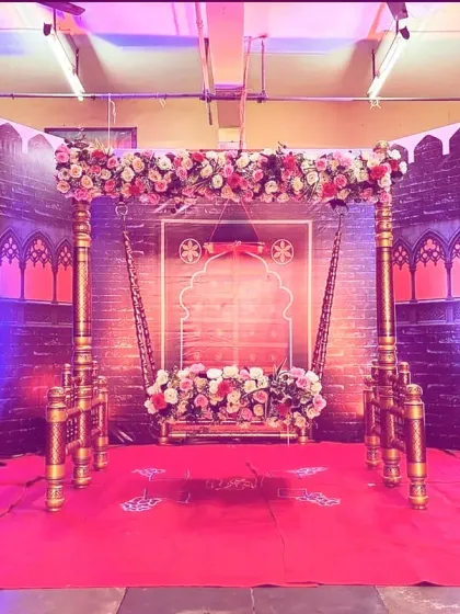 A traditional naming ceremony (naamkaran) setup featuring an ornate floral jhula (cradle) against a backdrop designed to look like a fort (gad).