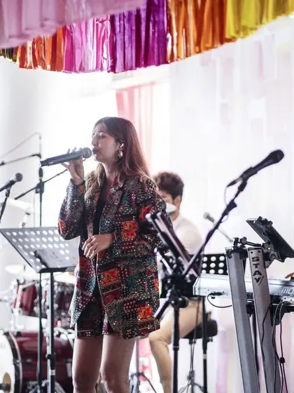 A live band performing at the Mehendi, adding to the festive and celebratory atmosphere. The backdrop features a soft, textured wall of white and pink.