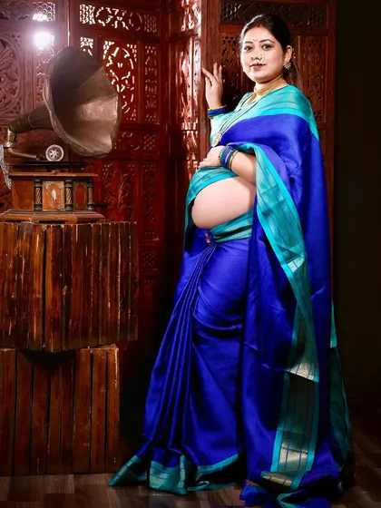 A full-length portrait incorporating a vintage gramophone. This prop adds a touch of nostalgia and artistry to the traditional saree maternity shoot.