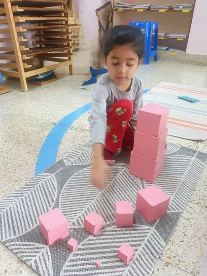 The iconic Pink Tower is a classic Montessori sensorial material. As this child carefully stacks the blocks from largest to smallest, they are visually discriminating dimensions, refining their motor control, and developing a mathematical mind.