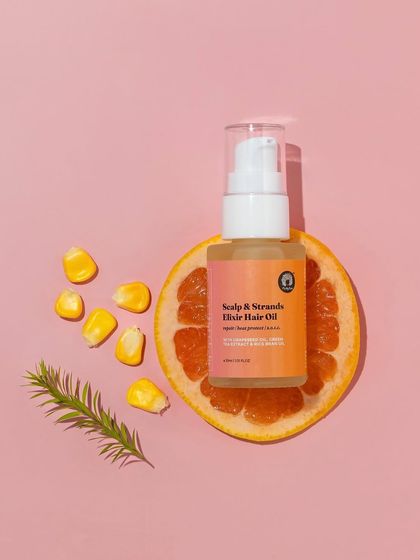 This top-down shot uses a slice of grapefruit as a natural pedestal for the hair oil. The simple composition on a pink background is clean, modern, and highlights the product's citrus notes.
