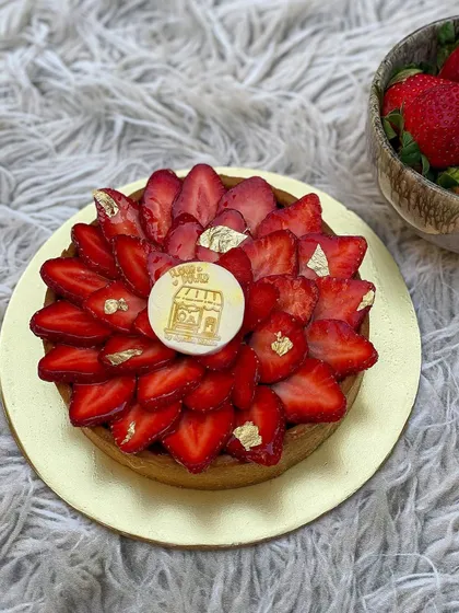 A stunning strawberry tart with gold leaf accents. The sweet pastry crust is filled with cream and topped with a beautiful arrangement of fresh strawberries.