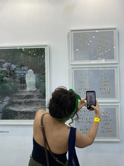 A visitor taking a photo of Surekha's work, which incorporates text and jasmine flowers.