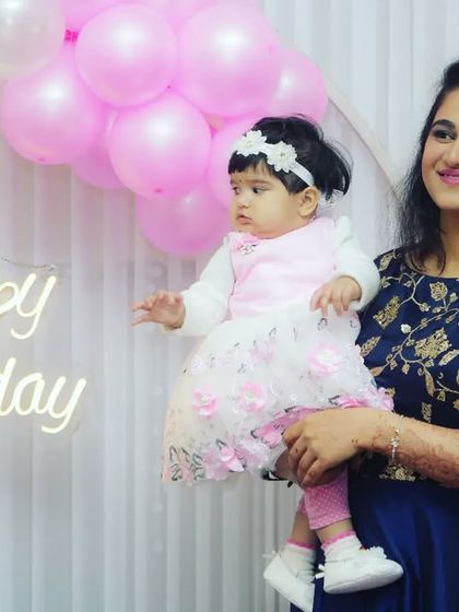 A mother holds her baby girl in front of a "Happy Birthday" sign. This photo beautifully combines the party atmosphere with a tender mother-daughter moment.