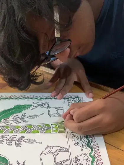 A close-up of the student working on his Madhubani piece, carefully adding details to the deer and fish, which are important symbols in the art form.
