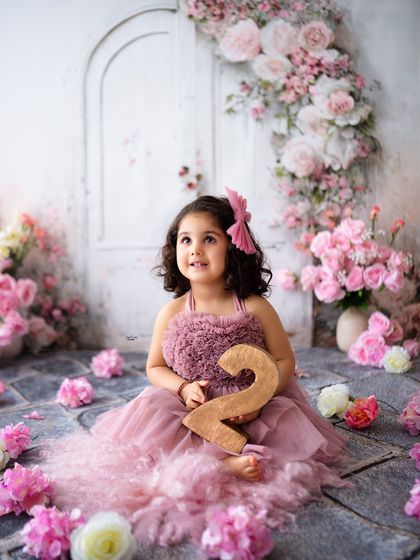 Looking up with wonder, this little girl holds the number '2' for her birthday portrait.