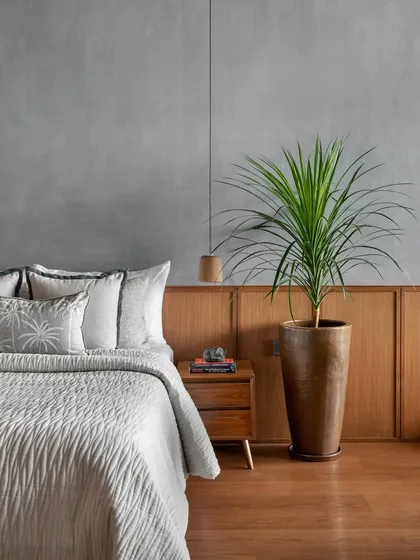 A detail of the reading bedroom, where a potted plant adds a touch of nature. The combination of the textured stucco wall, wood flooring, and simple furnishings creates a perfect environment for quiet contemplation.