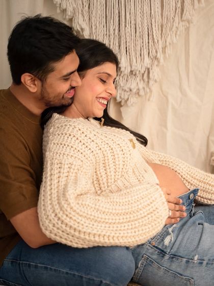 A tender moment between an expecting couple during their casual studio session. The partner leans in close with a smile, creating a feeling of warmth and intimacy.
