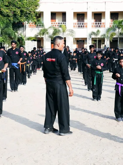 An instructor watches over a line of students, including a young girl with a purple belt, as they practice their forms.