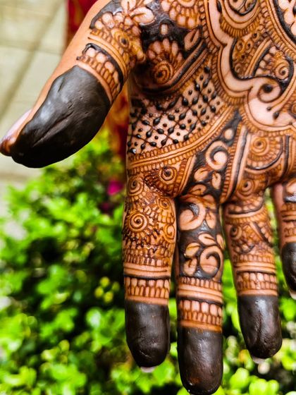 An extreme close-up of the fresh henna paste on the fingers, showing the texture and precision of the application.