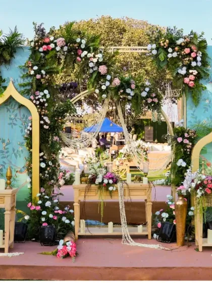 A beautiful setup for a welcome drink or dessert station. The pastel blue backdrop with golden arches and fresh flowers creates an elegant and inviting display.