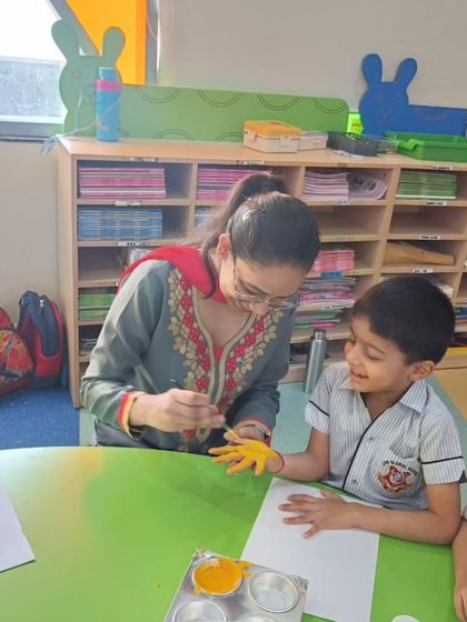 A teacher helps a student with a hand-painting craft, showcasing the personalized attention and encouragement we provide in our classrooms. These moments of guided creativity are precious.