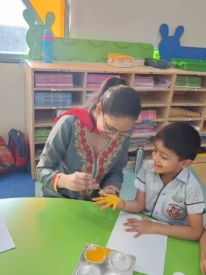 A teacher assists a student with his handprint art, a moment of guided creativity and bonding during our Mother's Day craft session.