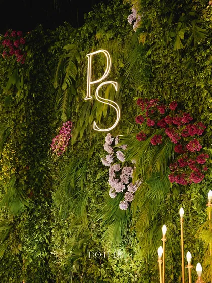 A modern and chic decor element for the Rishikesh Sangeet. A neon sign with the couple's initials is set against a lush green wall, creating a personalized and stylish photo backdrop.