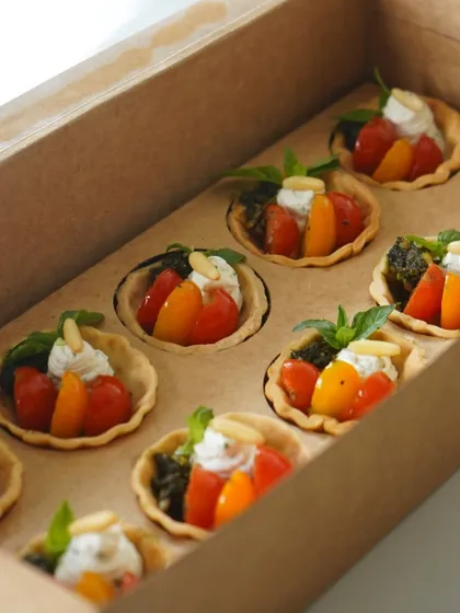 A box of our eggless cherry tomato and goat cheese tartlets, one of our best-selling items. These savory tarts are perfect for parties or as a light snack.