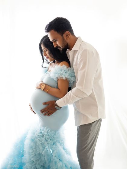 An intimate close-up of the couple, focusing on their connection as they both look down at the baby bump. The soft lighting highlights the beautiful details of the blue gown.