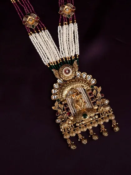 A close-up of the intricate pendant from the temple jewellery set, showing the detailed deity figure and surrounding stonework.