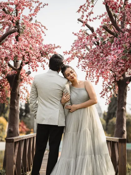 A serene pre-wedding moment captured on a bridge surrounded by cherry blossom-like trees. This showcases our ability to find picturesque natural settings for your shoot.