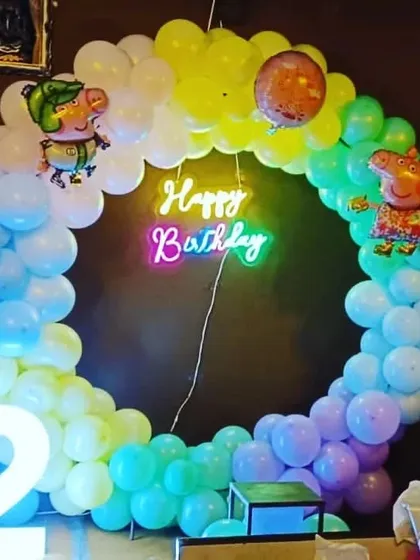 A fun Peppa Pig theme for a 2nd birthday. This decoration features a circular balloon arch in rainbow colors, a "Happy Birthday" neon sign, and Peppa Pig foil balloons.