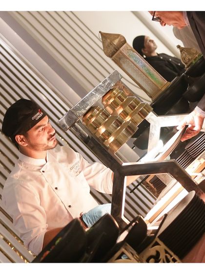 A chef operates a unique, vertical grilling apparatus, preparing specialty kebabs for a guest. We invest in innovative cooking equipment to provide distinctive culinary concepts and a memorable visual experience.