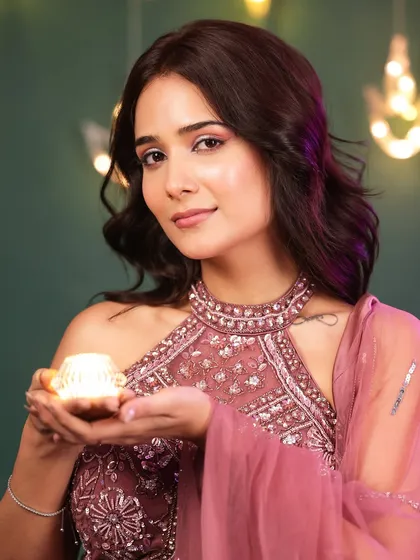 A beautiful portrait of the model holding a diya and looking at the camera, with festive lights creating a warm bokeh in the background.