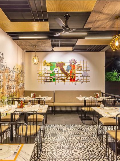 The outdoor seating area at Pasta Street, featuring a large, custom wall mural with iconic Italian symbols. The design combines rustic wall textures and patterned flooring with modern industrial chairs, creating a perfect blend of styles.