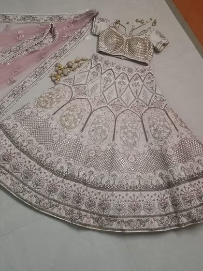 A flat-lay of the complete ivory and pink lehenga set. This view clearly displays the skirt's A-line cut, the blouse design, and the matching embroidered dupatta, helping you visualize the entire ensemble.