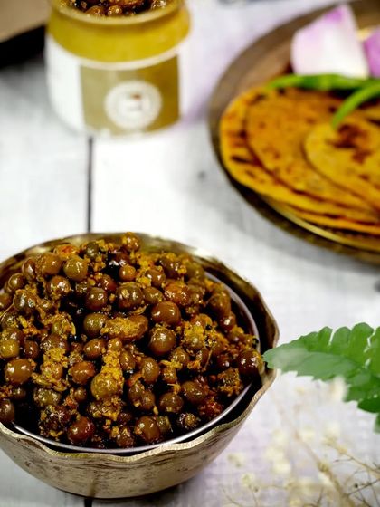 A traditional Indian pickle, "Teet Ka Achaar," is served in a brass bowl alongside fresh parathas. The composition creates a rustic and appetizing scene that feels like a homemade meal.