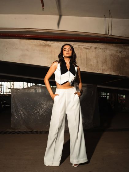 An edgy, on-location shoot with Anushka Sen in an industrial-style parking garage. The raw, concrete environment contrasts with her chic white outfit.