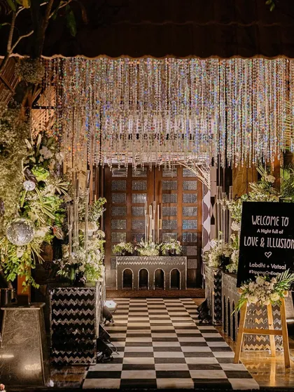 Welcome to a night of Love & Illusion. For this Sangeet, we designed a dramatic, high-concept monochrome entrance with a crystal curtain and checkerboard floor, setting the stage for an unforgettable party.