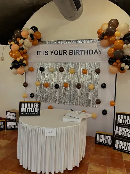 We had so much fun bringing the world of Dunder Mifflin to life for a fan's birthday. This setup features the iconic "IT IS YOUR BIRTHDAY" banner, a silver streamer backdrop, and custom Dunder Mifflin Paper Company props for a truly immersive themed party experience.