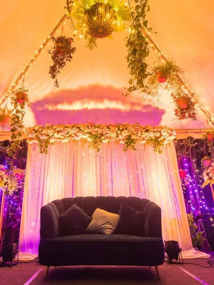 An intimate stage setup under a tent, illuminated with purple and orange lights, creating a cozy and magical ambiance for an evening event.