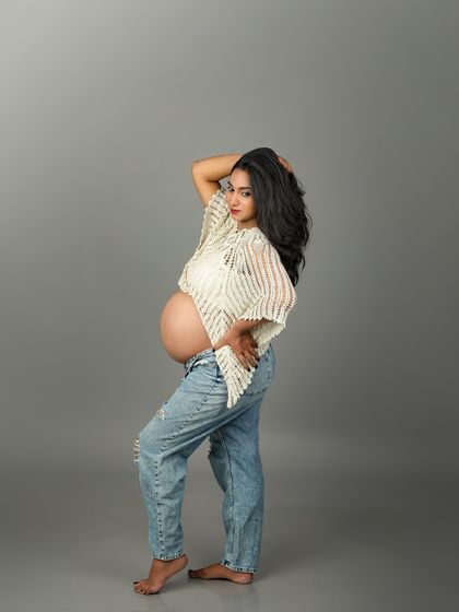 A confident and modern maternity pose. This mom-to-be shows off her bare bump with a casual top and ripped jeans, embodying strength and beauty.